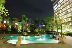 A swimming pool with a decorative edge, surrounded by palm trees and a building with illuminated windows. - Ijen Suites Resort & Convention (Klojen)