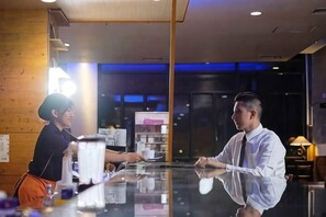 A bar area with a reflective surface, a counter, and a person standing behind it. - Ijen Suites Resort & Convention (Klojen)
