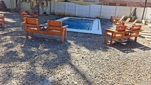 Zona de piscina con sillas de madera y una zona sombreada.