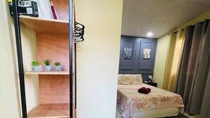 Un dormitorio con cama, mesita de noche, cómoda y estante con libros y objetos decorativos.