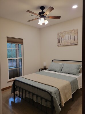 A bedroom with a bed, a nightstand, a lamp, a ceiling fan, and a window with blinds.
