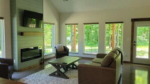 Ein geräumiges Wohnzimmer mit Kamin, bequemen Sitzgelegenheiten und großen Fenstern mit Blick ins Freie.