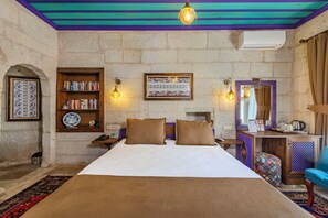 Una habitación de hotel con una cama grande, una estantería, un espejo decorativo y un escritorio con hervidor.