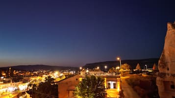 A nighttime view of a town with illuminated streets and buildings, a prominent hill in the background, and a large rock formation on the right.
