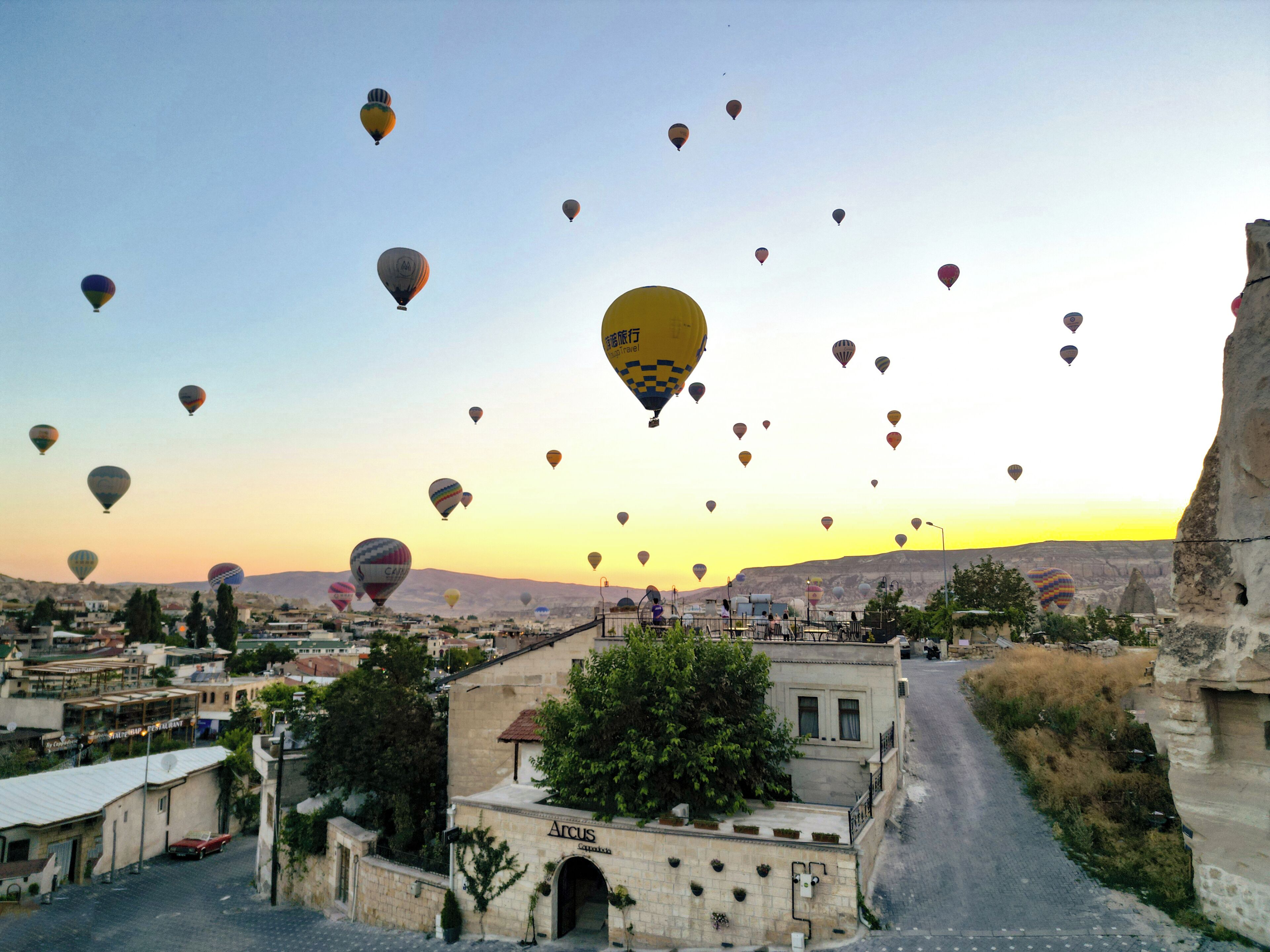A street with buildings and a clear sky with hot air balloons.