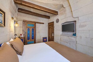 Una habitación con una cama, una puerta de madera, un televisor montado en la pared y una lámpara.