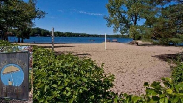 Una spiaggia con una rete da pallavolo, un cartello con un logo e un corpo d'acqua sullo sfondo.