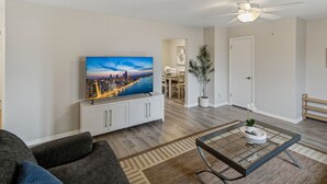 Un soggiorno con una TV a schermo piatto, un divano, un tavolino da caffè, una ventola a soffitto e un'area pranzo sullo sfondo.