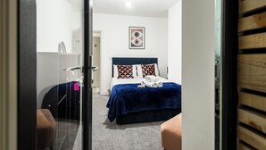 A hotel room with a bed, a blue blanket, and a door leading to another room.