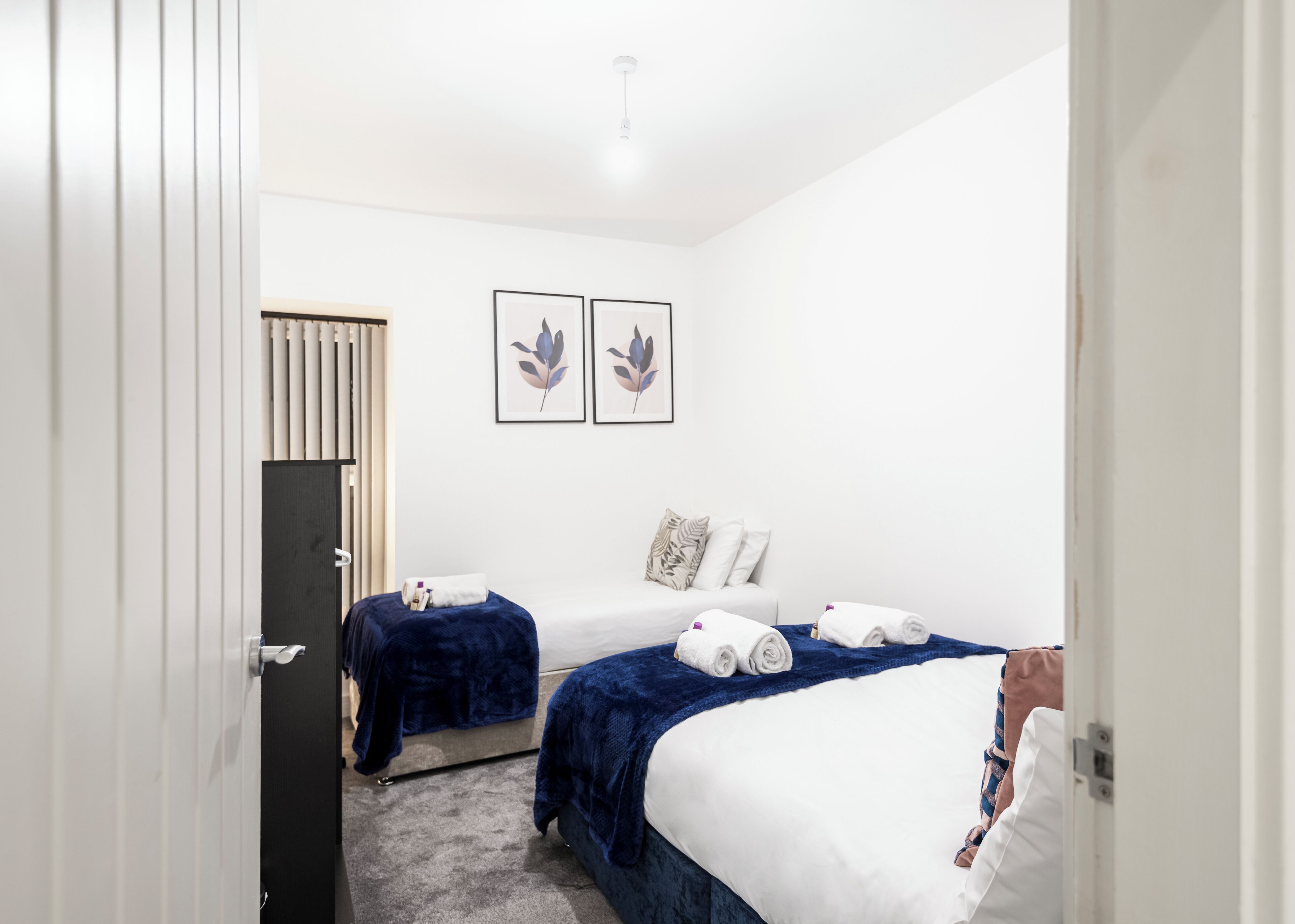 Ett hotellrum med två sängar, en garderob och två inramade konstverk med lövmotiv på väggen.