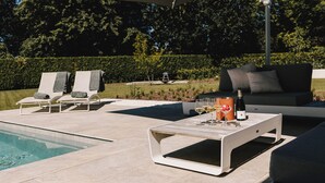 Un espace aménagé au bord de la piscine, avec des chaises longues, une table avec des boissons et un canapé placé sous un grand parasol.