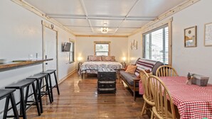 A cozy room with a bed, a sofa, a dining table with chairs, and a bar area with stools. - The Sunset Retreat Cabin (Monticello)