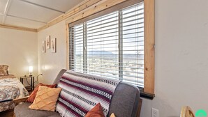 A room with a bed, a sofa, a window with blinds, and a small table with a lamp. - The Sunset Retreat Cabin (Monticello)