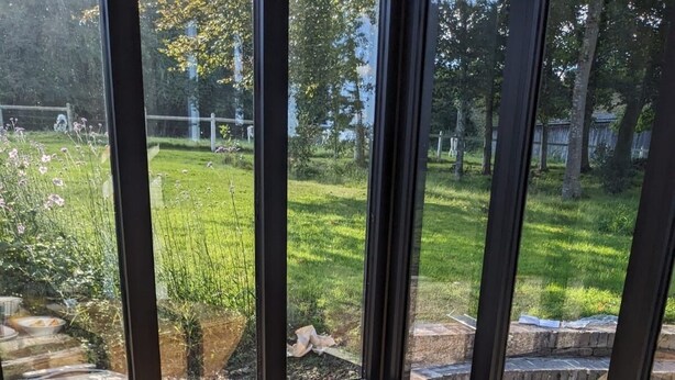 Taula de matí amb menjar, un got de suc i vista a un jardí a través de grans finestres.