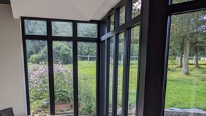 Zona de menjador amb una taula rodona i cadires, grans finestres que donen a un jardí.