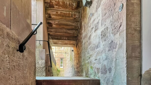Una estrecha escalera de piedra con barandilla de madera que lleva a una puerta.