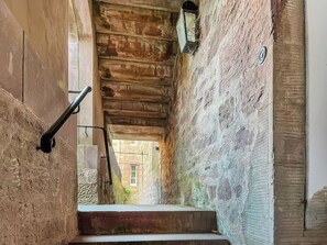 Una stretta scala in pietra con ringhiera in legno, che conduce a un portale.