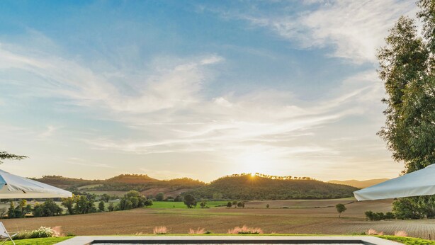 A pool area with a view of rolling hills and a sunset. There are three bean bags and a lounge chair. - Casale Rondinella 6+2, Emma Villas (Manciano)