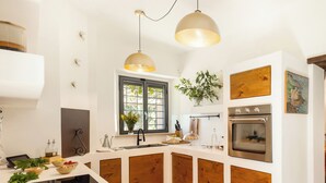 A modern kitchen with a central island, wooden cabinets, a built-in oven, and pendant lighting. - Casale Rondinella 6+2, Emma Villas (Manciano)