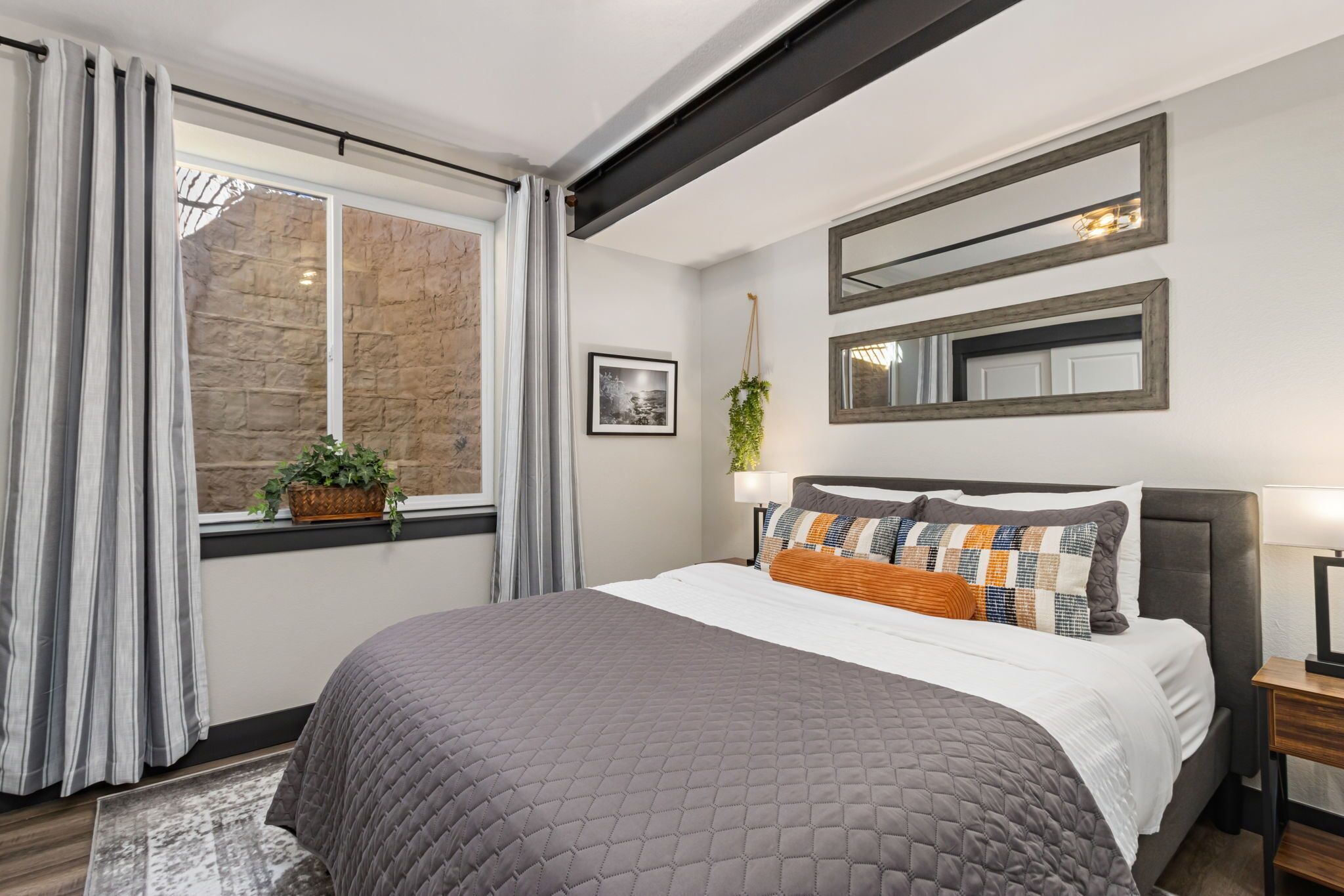 Un dormitorio con una cama grande, una ventana con cortinas, un muro de piedra y una planta colgante.