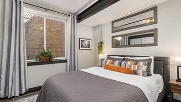 Un dormitorio con una cama grande, una ventana con cortinas, un muro de piedra y una planta colgante.