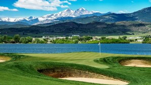 Ein Golfplatz mit einer Fahne, einem See und Bergen im Hintergrund.