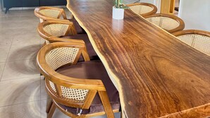 A spacious dining area with a long wooden table, wicker chairs, and a chandelier.