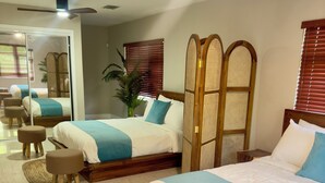 A modern hotel room with two beds, a large mirror, a ceiling fan, and a potted plant.