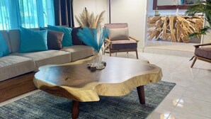 A modern living room with a wooden coffee table, a sofa with blue and brown cushions, a chair, and a decorative plant.