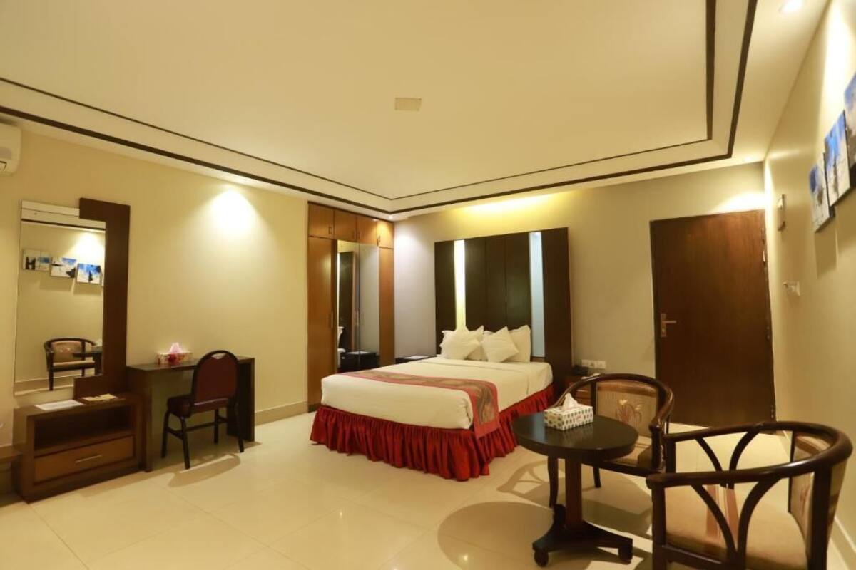 A hotel room with a bed, a desk, a chair, a table, and a wardrobe.