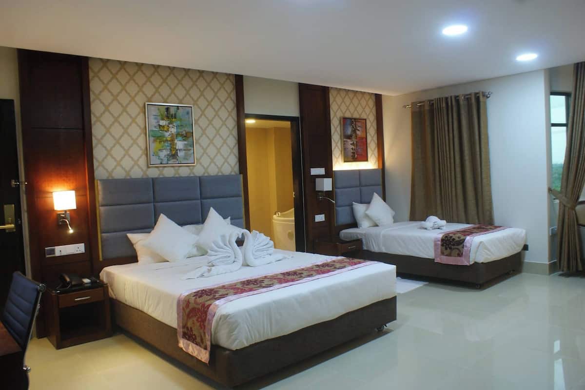 A hotel room with two beds, a nightstand with a phone, and a wall-mounted lamp.