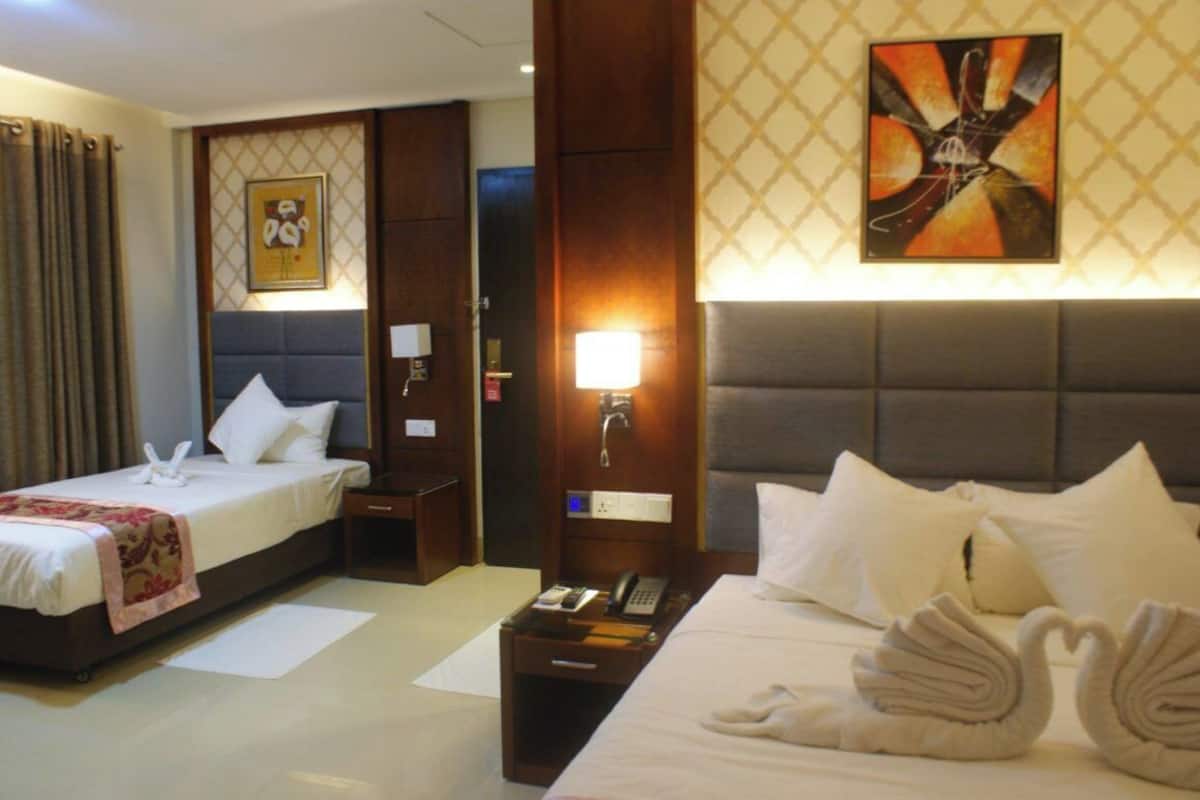 A hotel room with two beds, a nightstand with a phone, a wall-mounted lamp, and artwork.