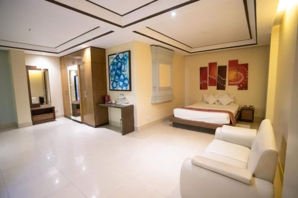 A modern hotel room with a large bed, a sitting area, a desk, and a wardrobe.