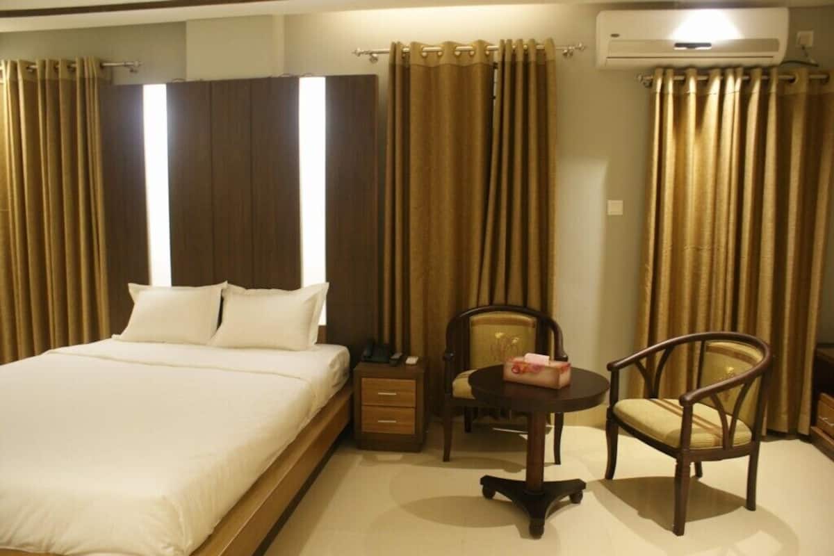 A hotel room with a bed, a bedside table with a lamp, a chair, and a small table with a chair.