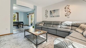 Una sala de estar moderna con un sofá de cuero gris, una mesa de centro de madera y decoración en la pared.