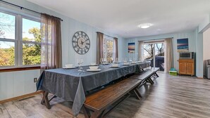 Un comedor con una mesa larga dispuesta para una comida, un reloj en la pared y vistas al exterior.