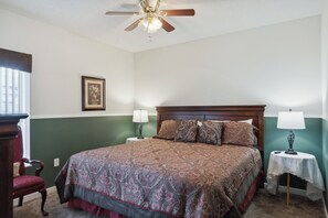 A bedroom with a bed, two bedside tables, a chair, a ceiling fan, and a framed picture on the wall.