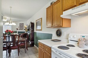 A kitchen with wooden cabinets, a white stove, and a dining area with chairs and a table.