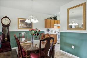 A dining area with a wooden table, chairs, a vase of flowers, a clock, and kitchen cabinets. - 2 Bedroom, Indoor Pool, King Beds, Downtown (Pigeon Forge)