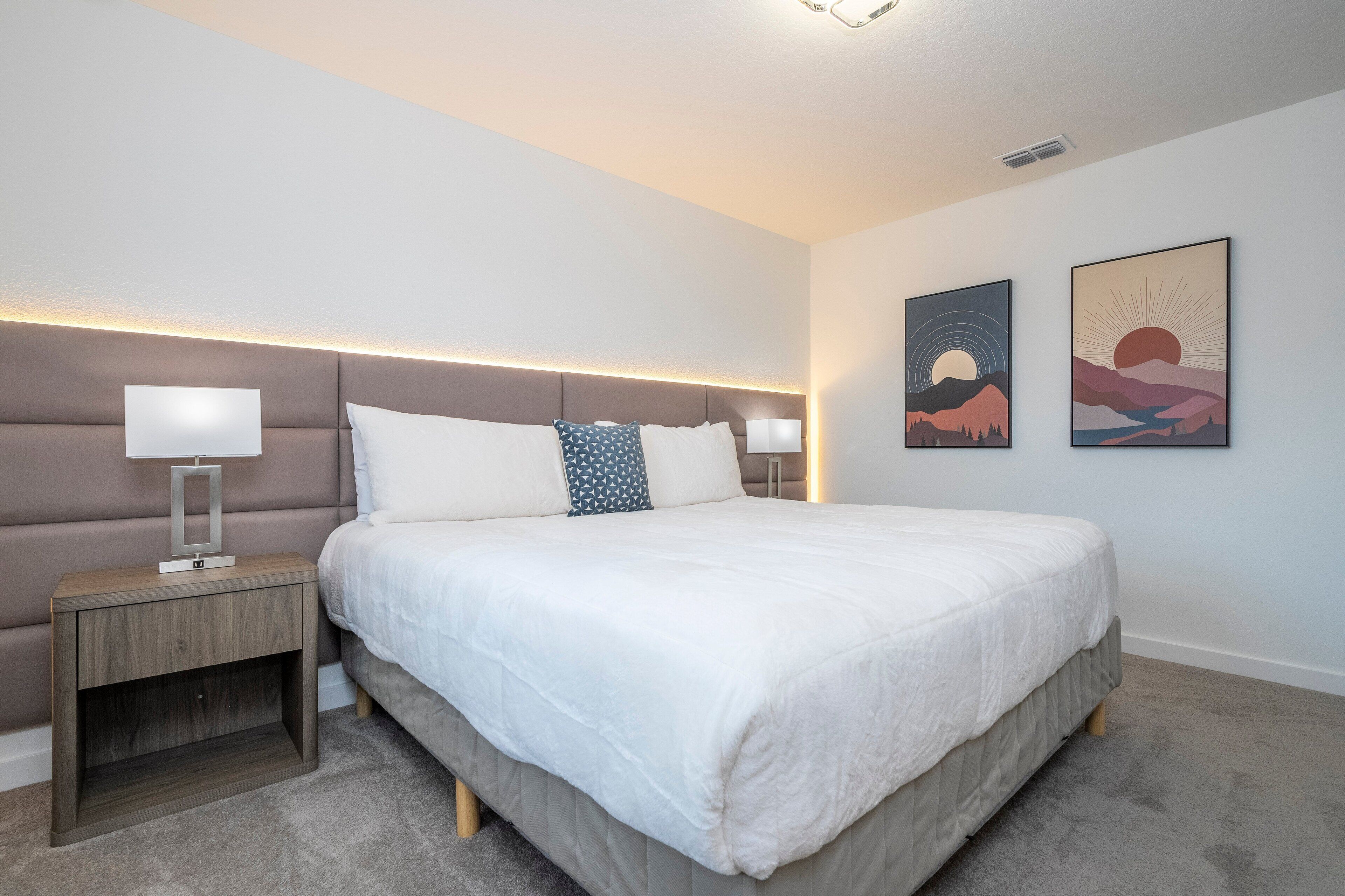 A modern bedroom with a large bed, a bedside table, and two wall-mounted artworks.