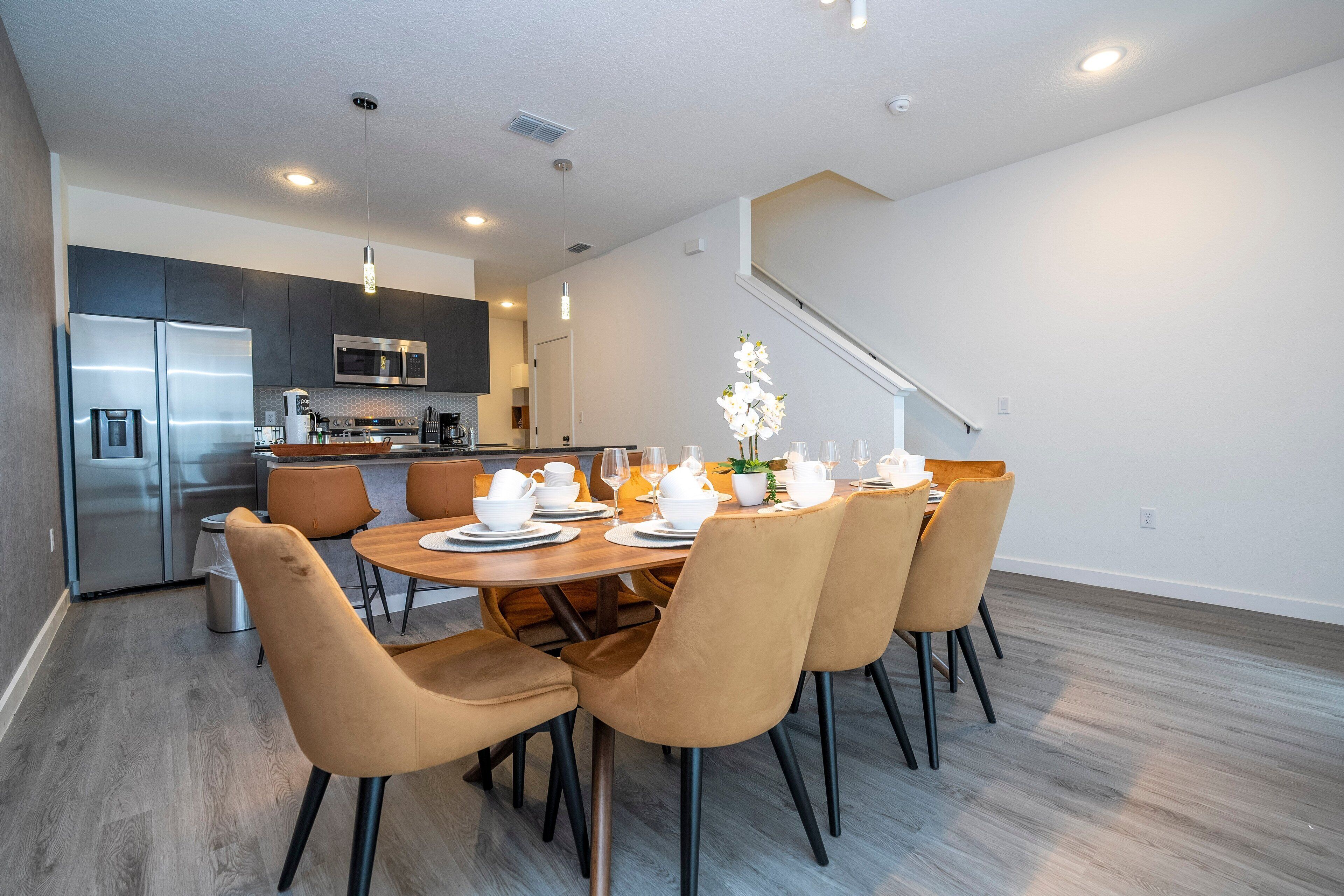 A modern kitchen with stainless steel appliances, a dining area with a wooden table and chairs, and a staircase leading to another level.