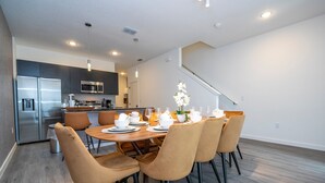Una cocina moderna con electrodomésticos de acero inoxidable, un comedor con mesa y sillas de madera, y una escalera que sube a otro nivel.