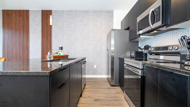 Una cocina moderna con armarios oscuros, electrodomésticos de acero inoxidable y suelo de madera.