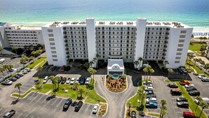 Un hotel de varios pisos con patio central, estacionamiento y vista al océano.