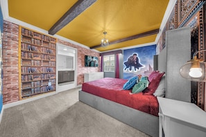 Un dormitorio con una gran estantería, una cama con ropa de cama roja y un mural en la pared.