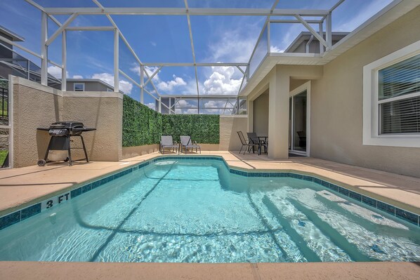 A swimming pool with a glass ceiling, surrounded by a beige wall and a green hedge.