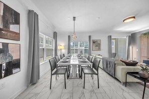 A modern dining area with a long table, chairs, and a chandelier.