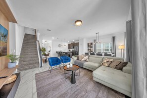 A spacious living area with a sofa, two blue chairs, a coffee table, and a staircase leading to a kitchen. - 1010 SS - Modern Comfort Oasis (Four Corners)