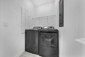 A laundry room with two stacked washers and dryers, a metal drying rack, and a door with a handle. - 1010 SS - Modern Comfort Oasis (Four Corners)