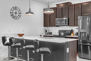 A modern kitchen with dark wooden cabinets, stainless steel appliances, a central island with bar stools, and pendant lighting. - 1010 SS - Modern Comfort Oasis (Four Corners)